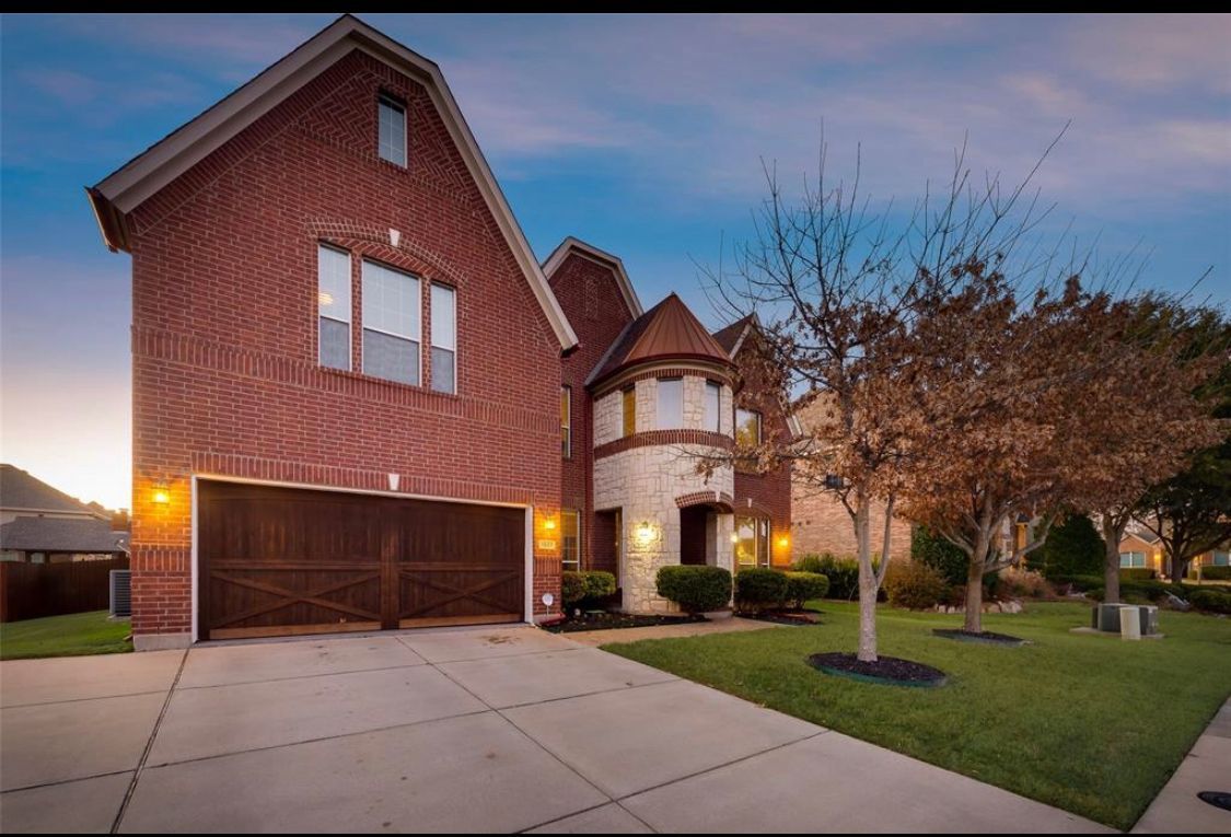 Brick house with a two-car garage, stone facade, and a well-manicured lawn under a dusky sky.