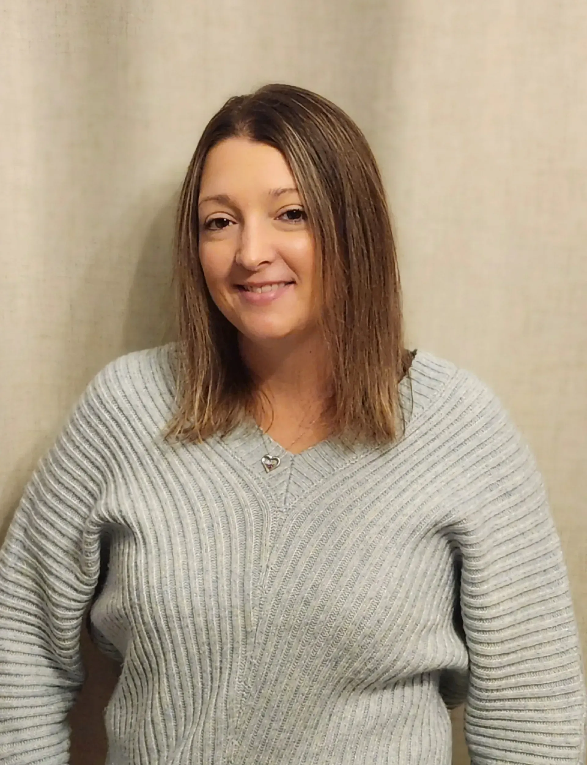 Woman in a gray sweater smiling against a beige curtain backdrop