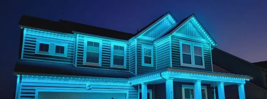 A house outlined in bright blue neon lights at night, with a dark sky overhead.
