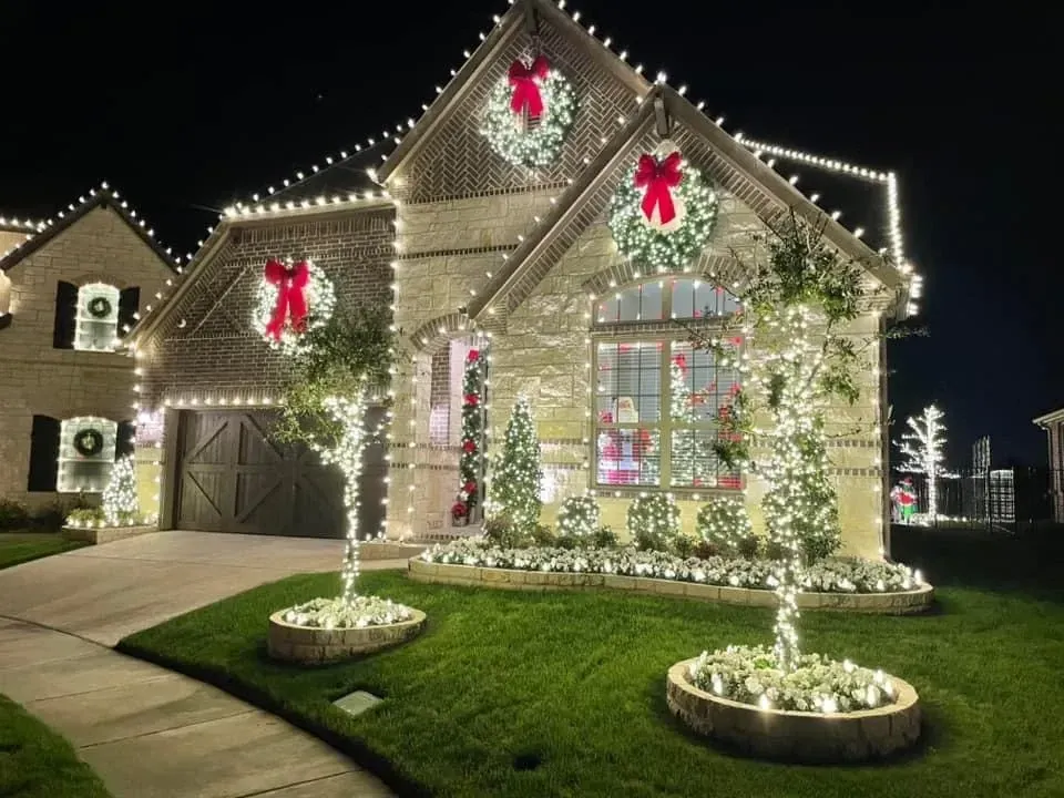 House exterior decorated with white Christmas lights and red bows at night