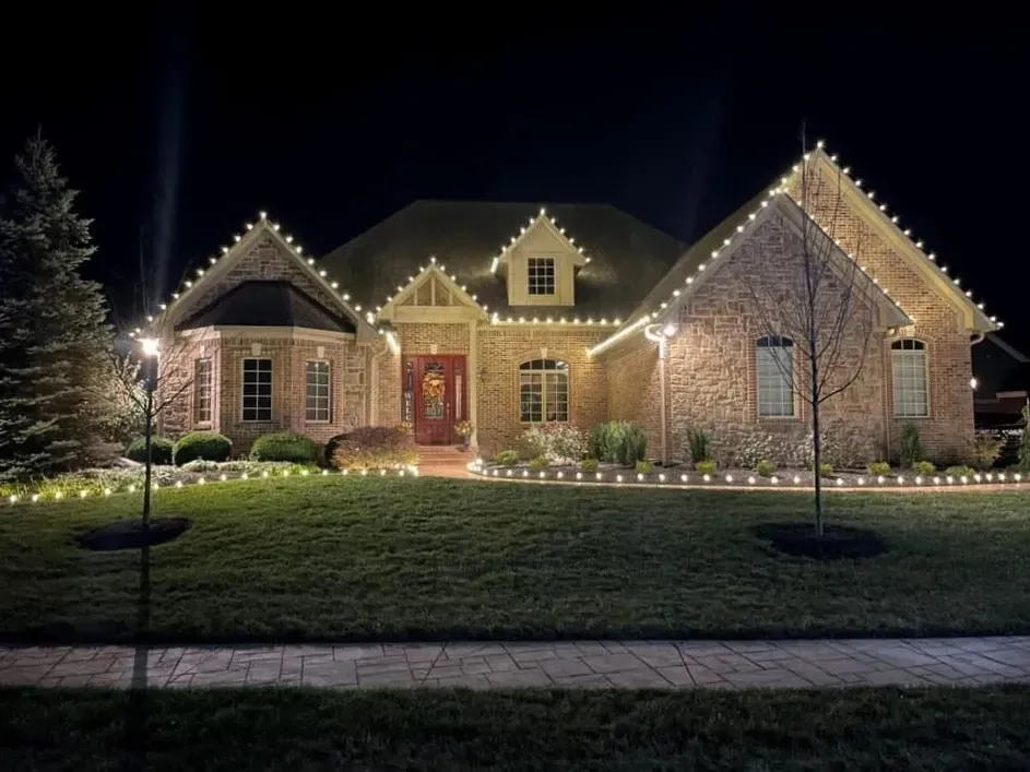 Brick house lit with white holiday lights at night, with a manicured lawn and walkway.