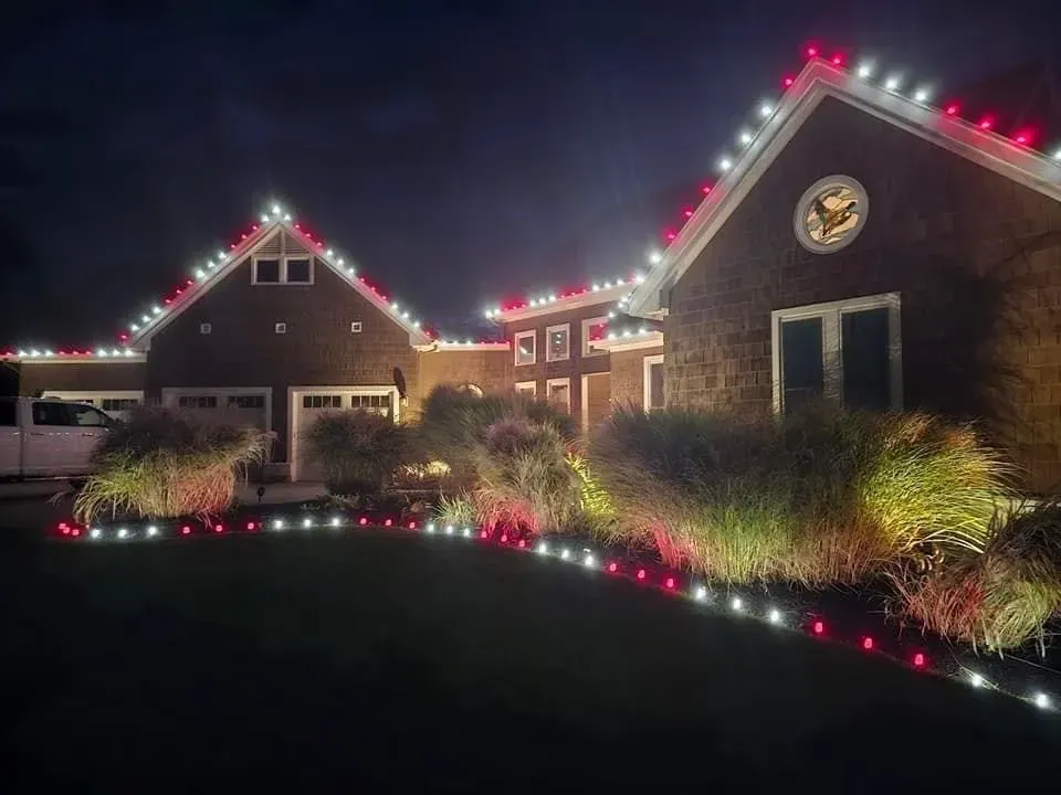 Brick houses outlined with red and white holiday lights along a dark driveway at night