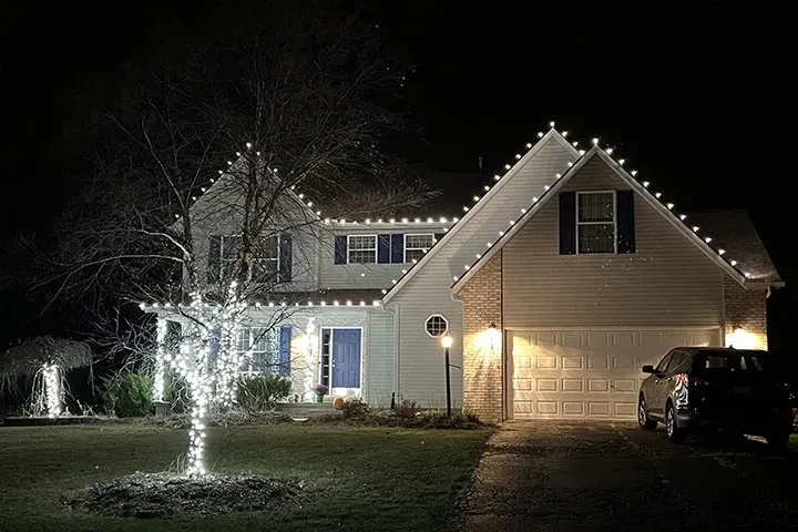 Lit house at night with Christmas lights, a glowing front yard tree, and a car in the driveway