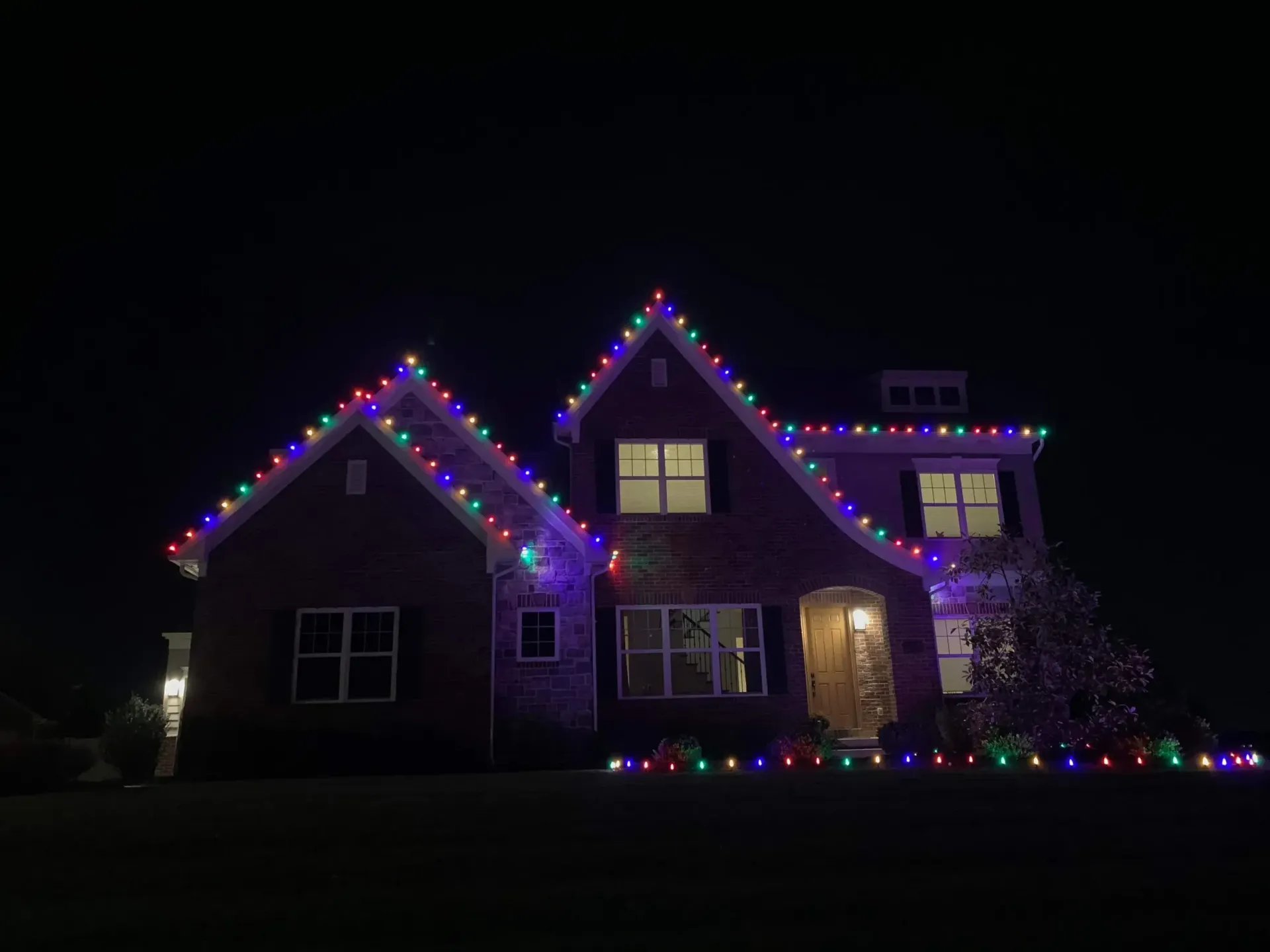 House at night outlined with colorful Christmas lights and lit windows.