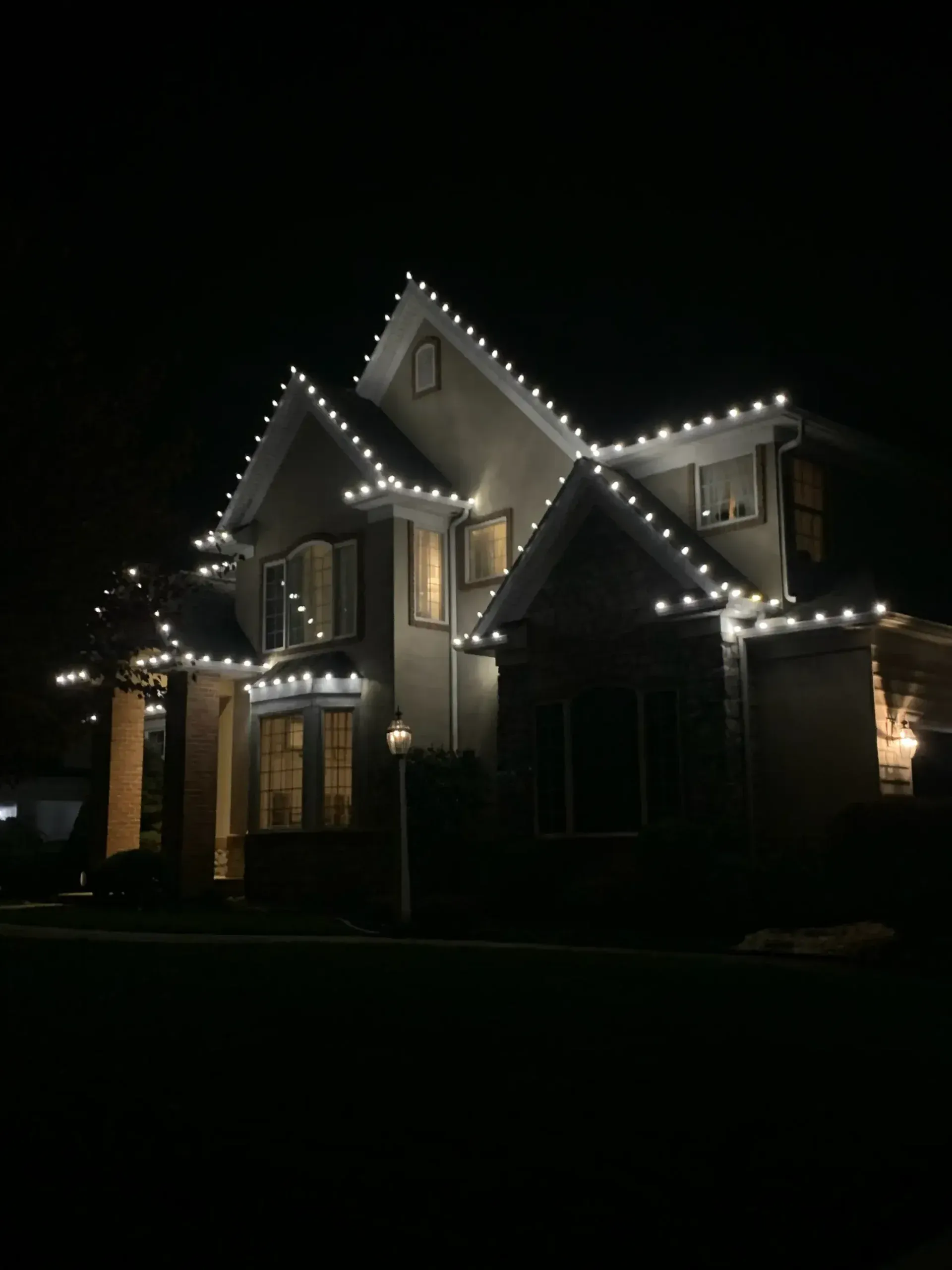 Large two-story house at night, outlined with white string lights against a dark sky.