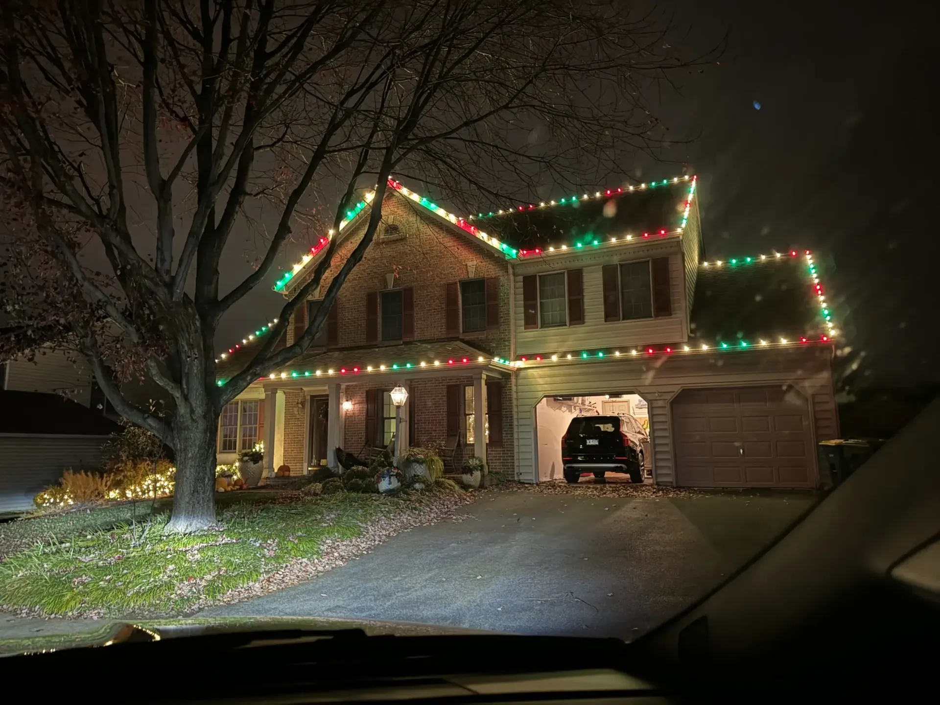 Two-story house decorated with red and green Christmas lights at night, seen from a driveway