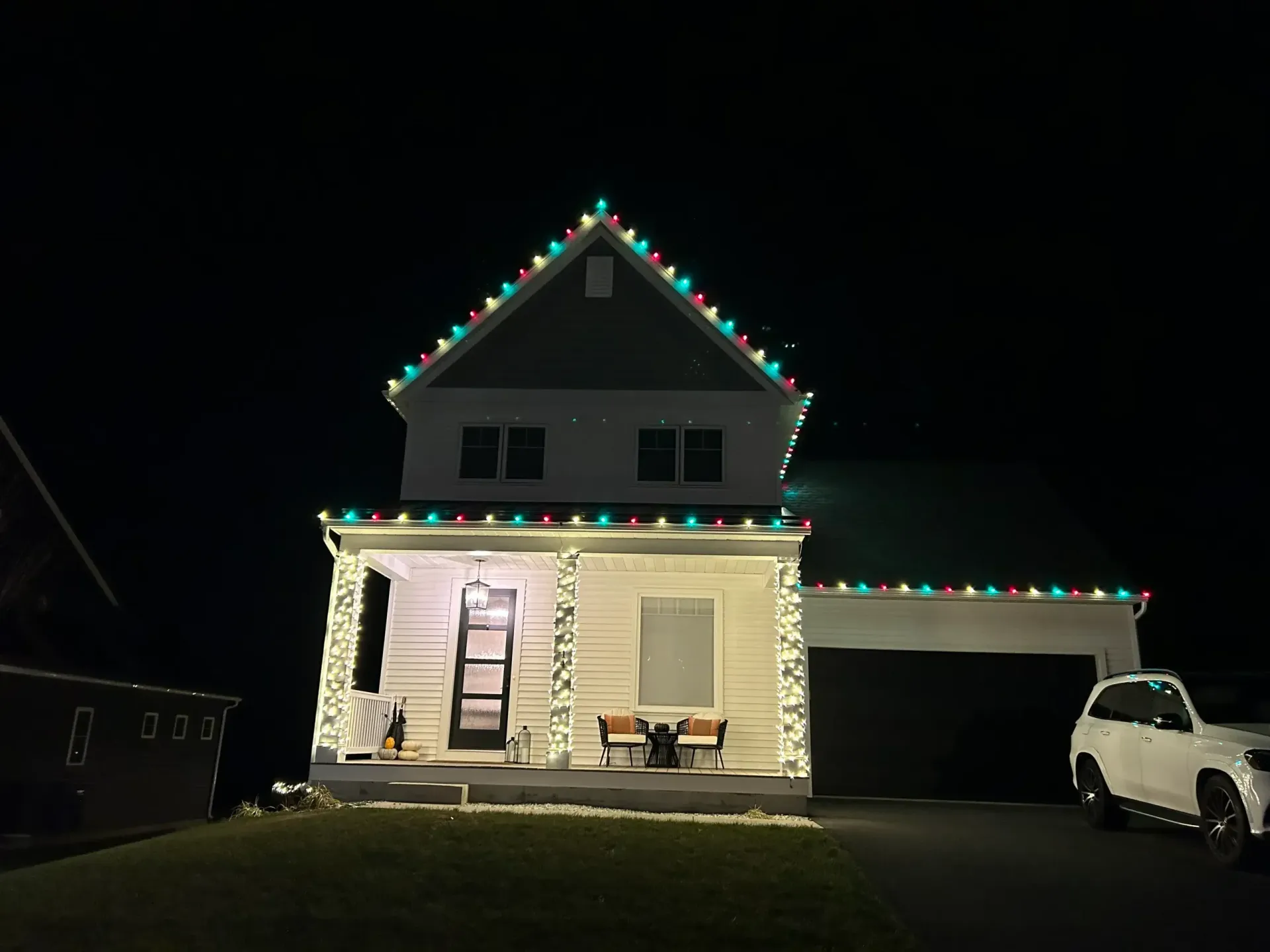 House at night with colorful roof lights, lit porch, and a white SUV in the driveway.