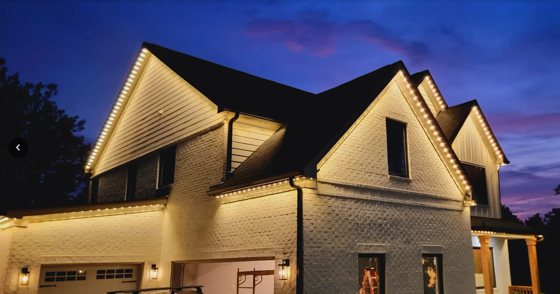 Illuminated white house with steep gabled roof at dusk against a purple-blue sky