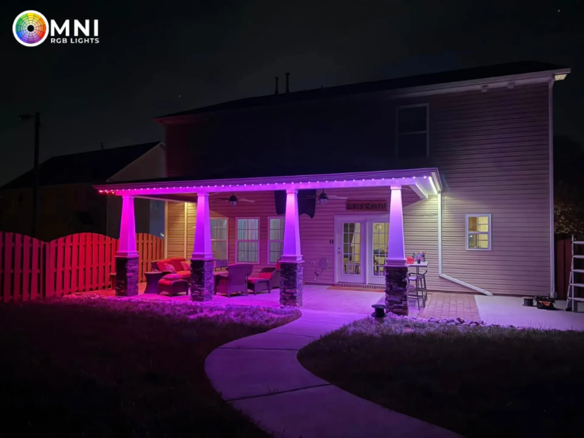 House exterior lit with purple and pink lights at night, with a curved walkway leading to the porch