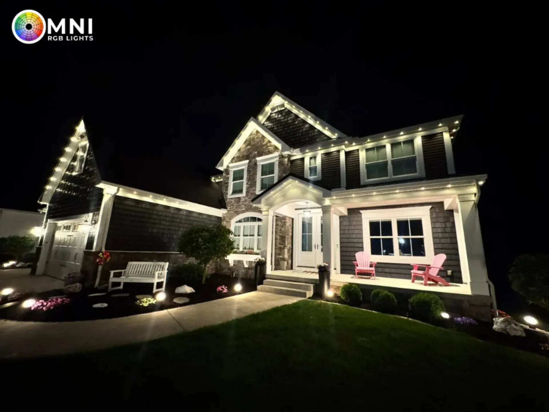 Nighttime view of a lit two-story house with white trim, a driveway, and a pink bench on the porch