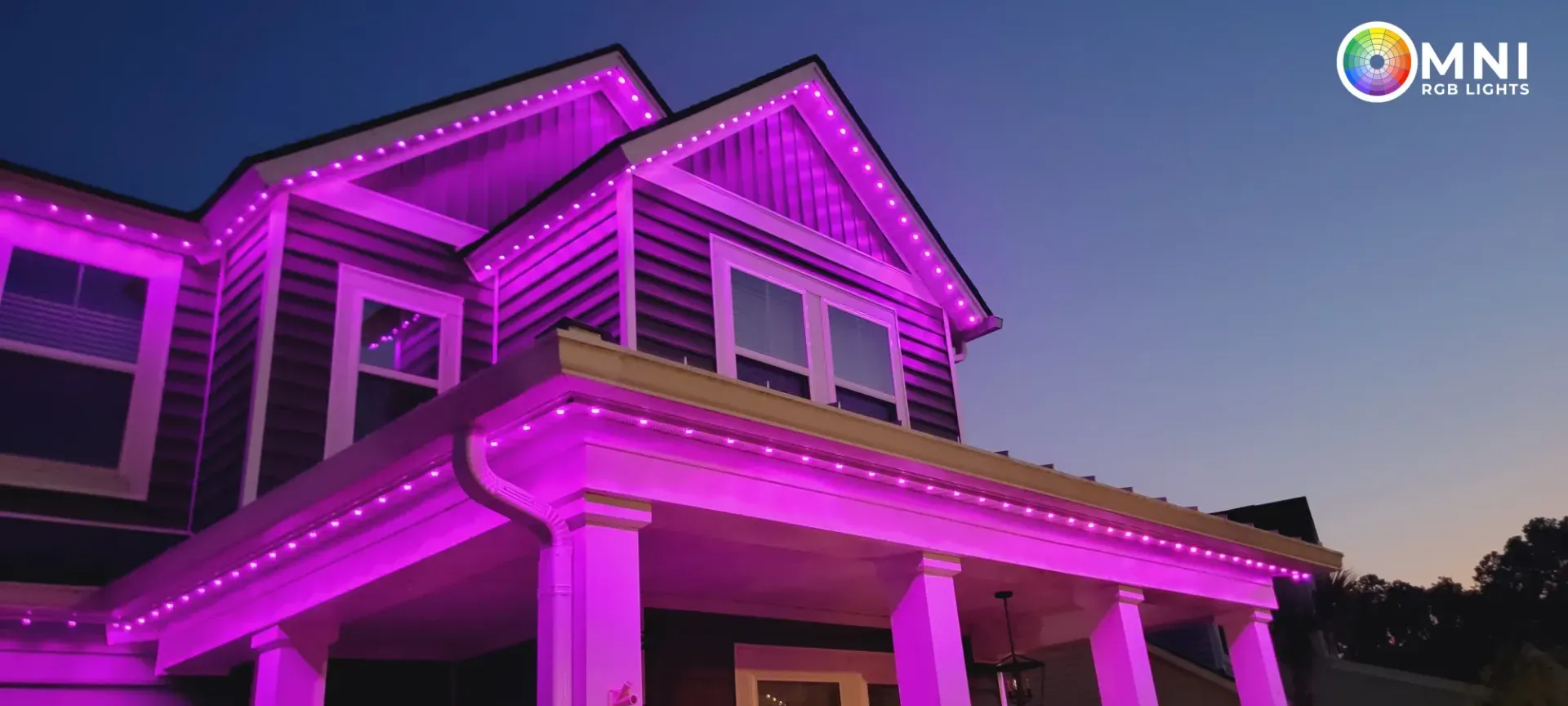 Two-story house lit in bright purple at dusk with a visible roofline and porch columns