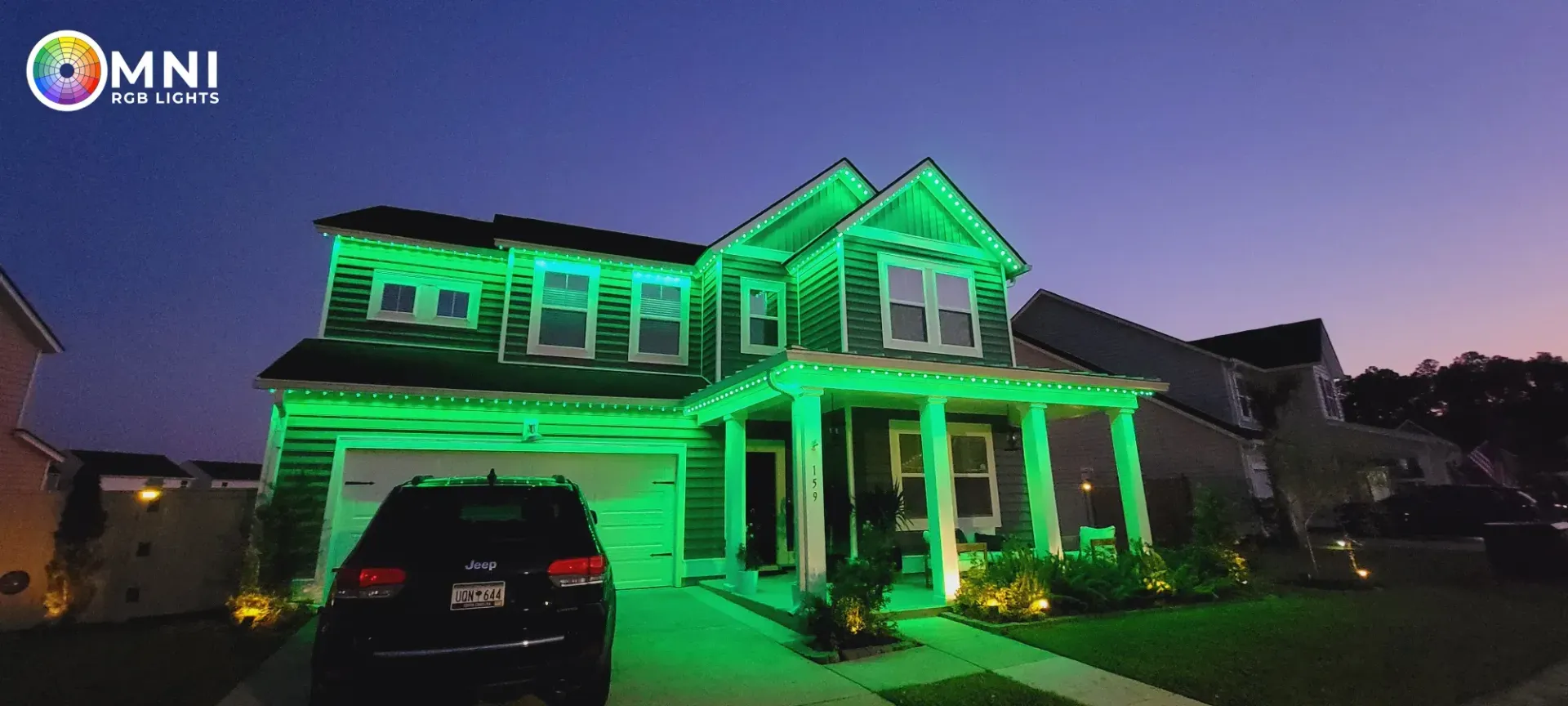 Two-story house lit in bright green at dusk, with a car parked in the driveway.