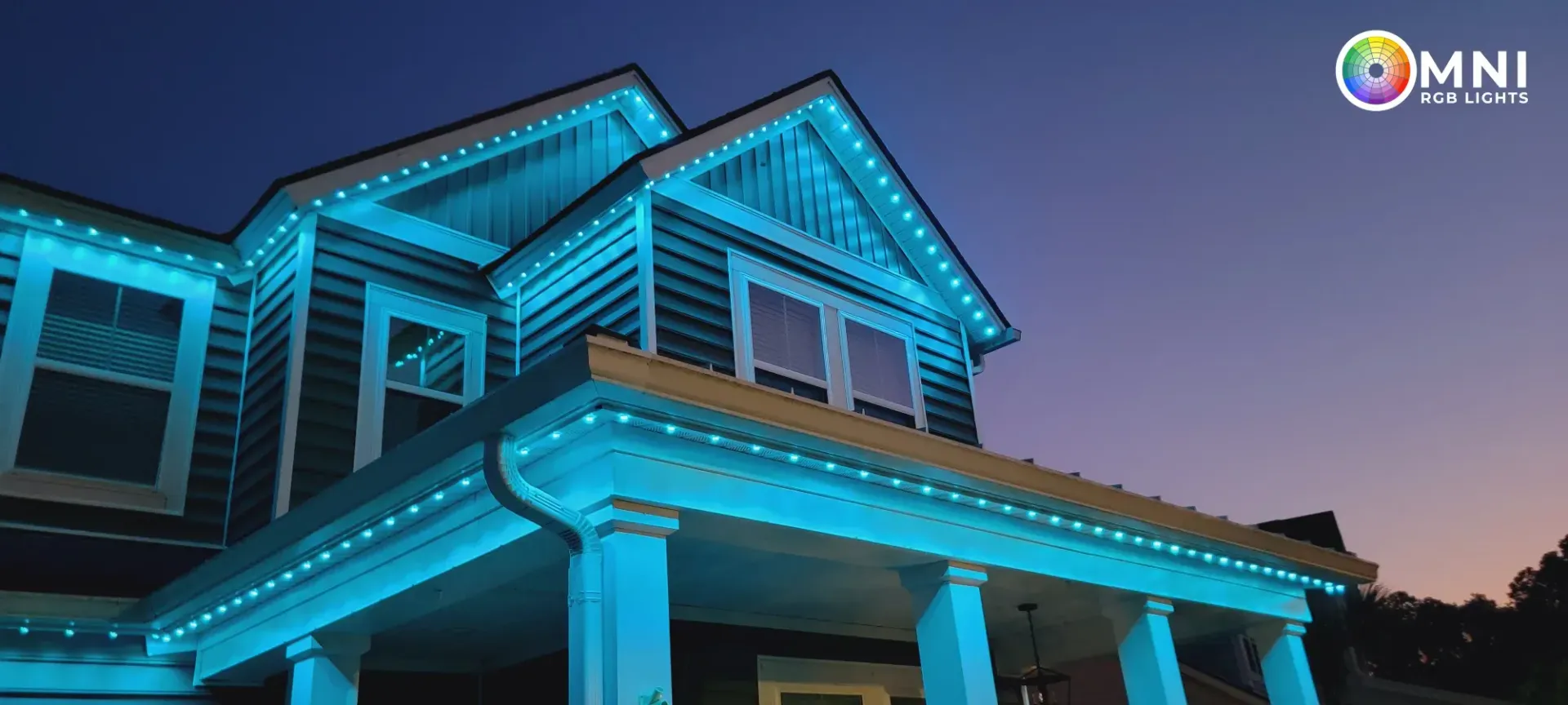 Blue-lit modern house at dusk with illuminated porch and roofline against a twilight sky