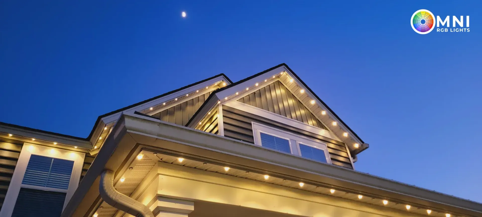Nighttime view of a lit building facade with a peaked roof against a deep blue sky