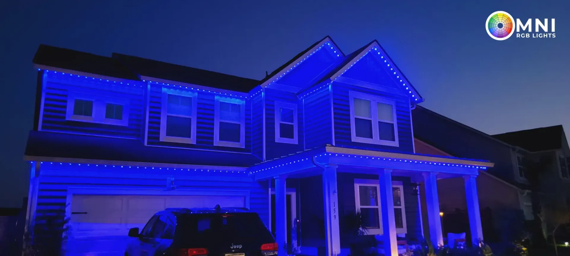 Two-story house lit in blue at night, with a car parked in the driveway.