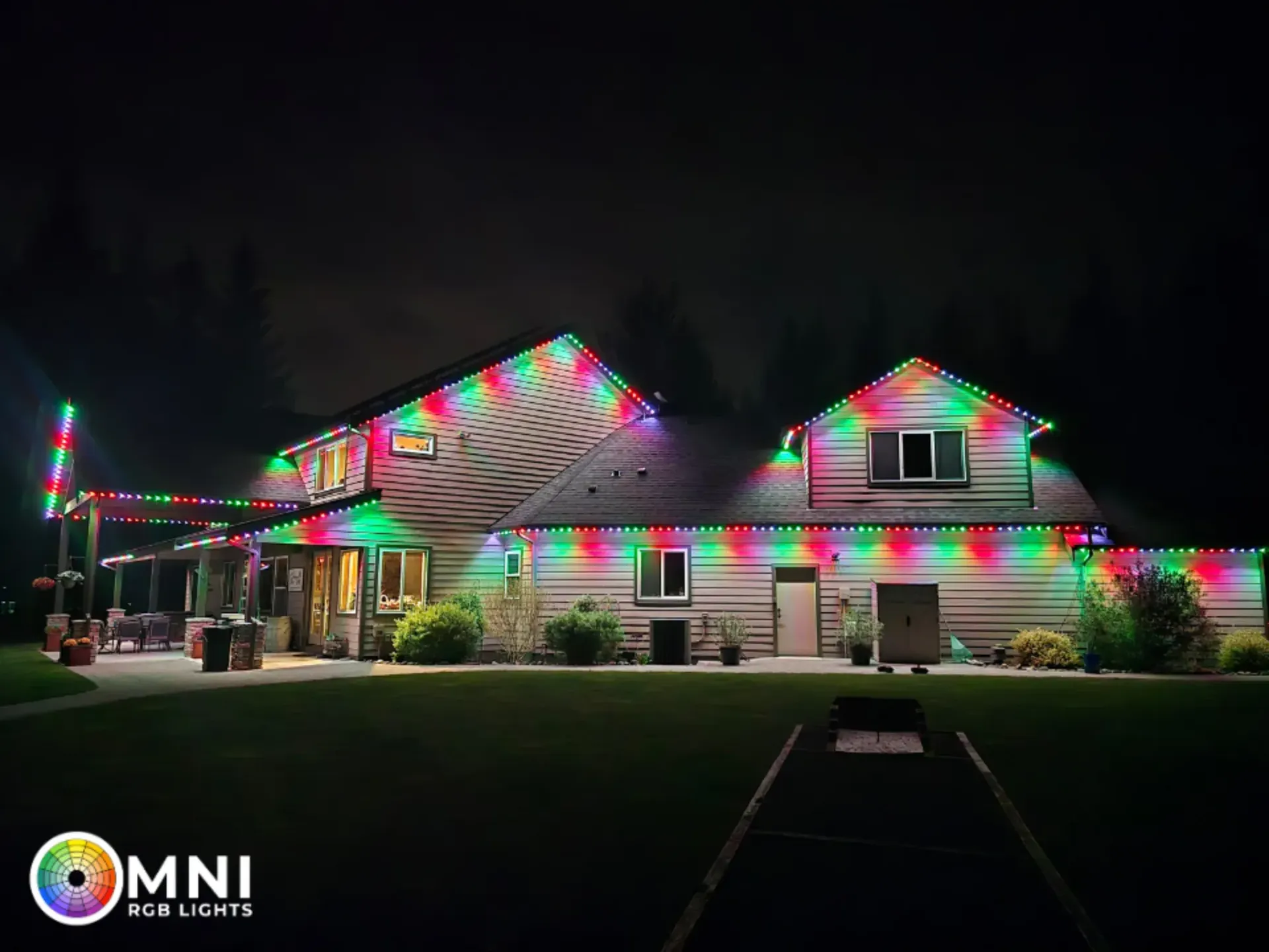 Single-story house decorated with colorful Christmas lights at night, with a lit lawn and dark sky.