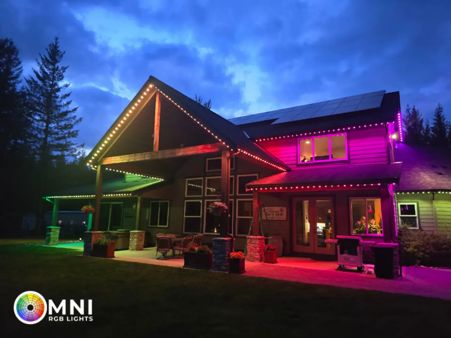 House illuminated with colorful LED lights at night, glowing pink, green, and purple against a dark sky