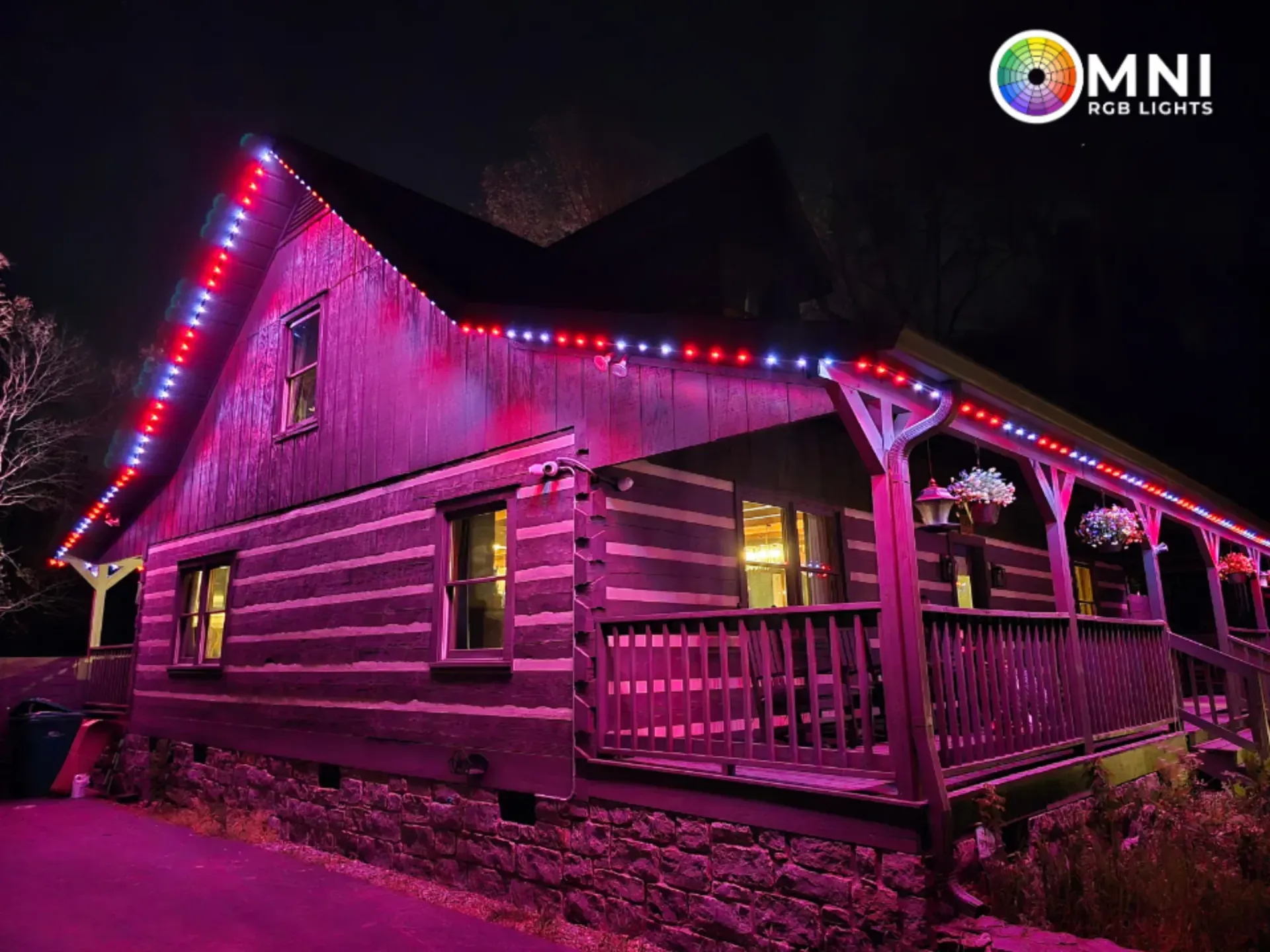 Log cabin at night lit with pink and red string lights, with a porch and glowing windows.