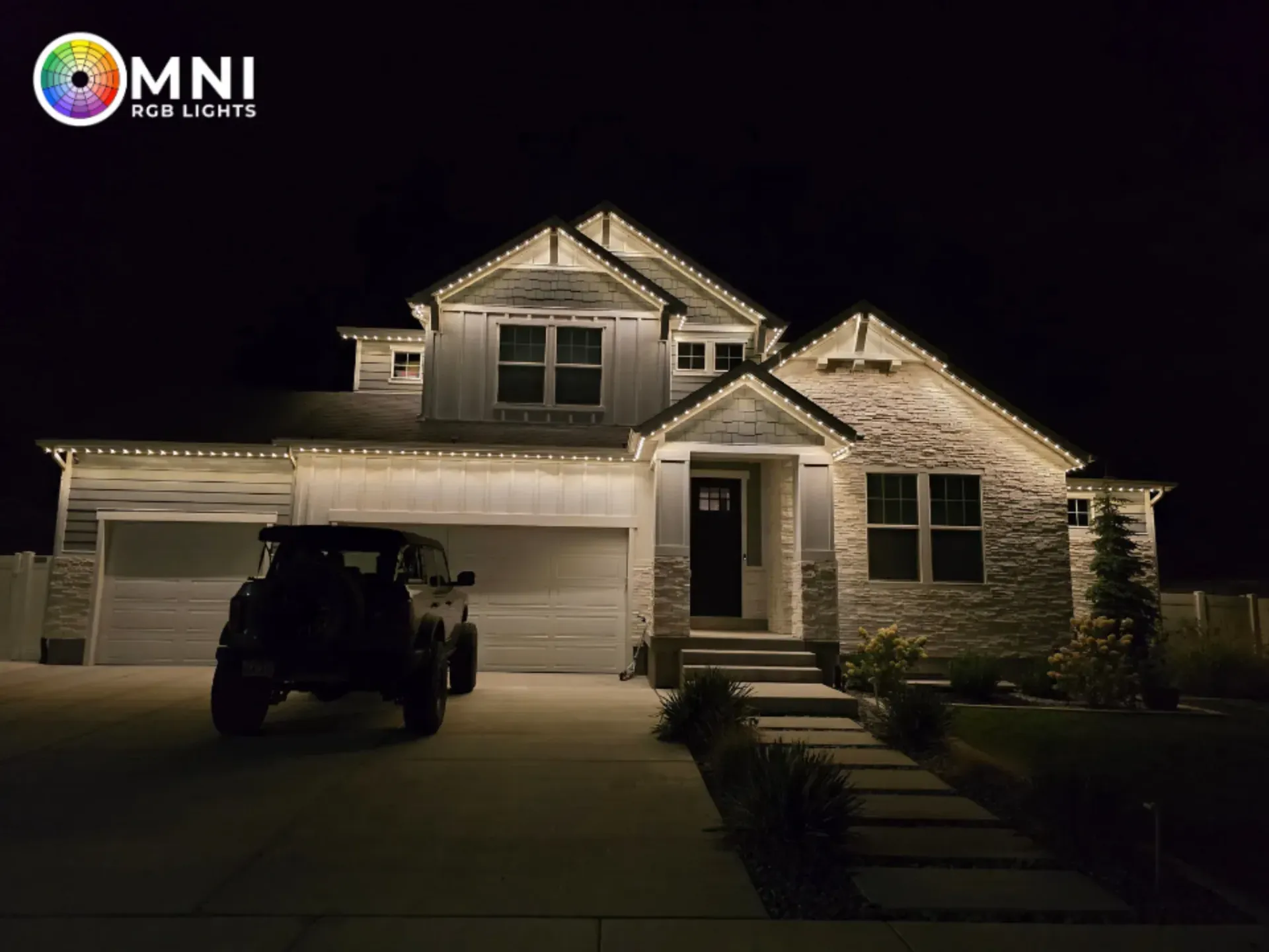 Two-story suburban house at night, warmly lit exterior with a car in the driveway.