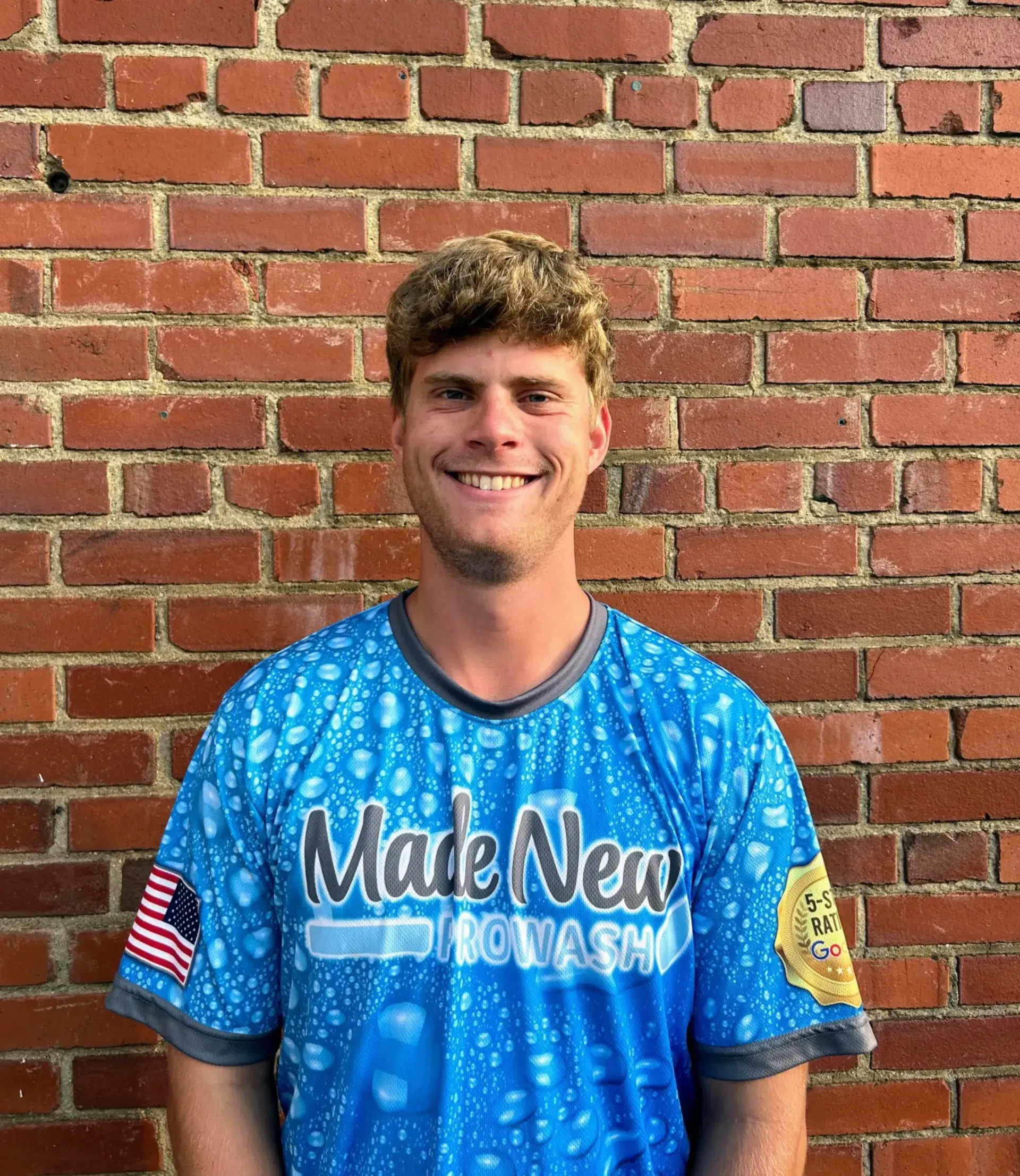 Smiling person in a blue jersey standing against a red brick wall
