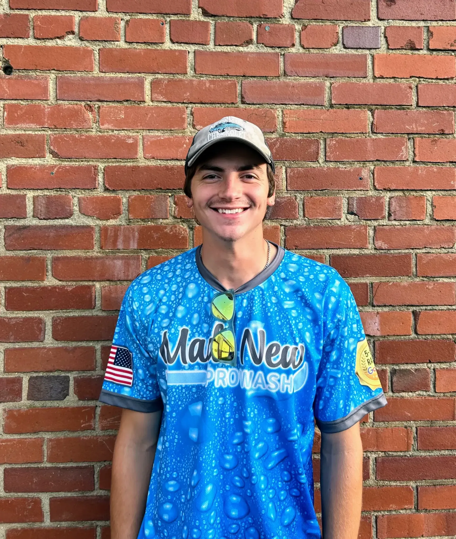 Smiling person in blue Miami jersey and cap standing against a brick wall.