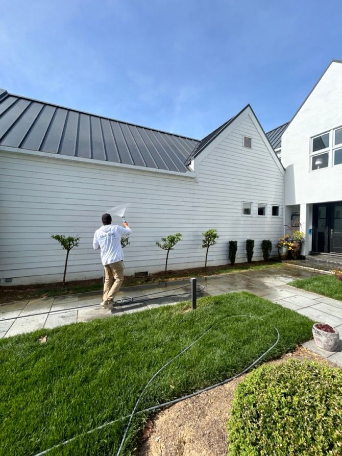 Person walking along a path beside a white building with a dark roof and small trees.