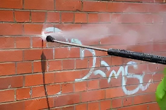 Pressure-washing white graffiti from a red brick wall