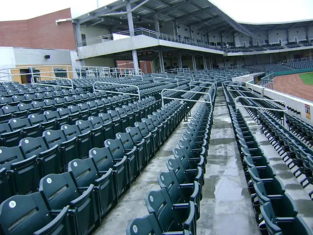 Empty stadium seating under a covered grandstand, with rows of dark green chairs and a concrete aisle
