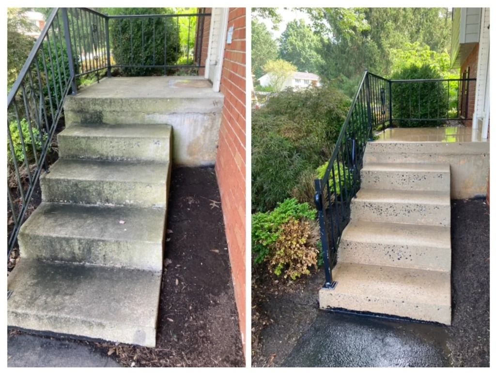 Outdoor concrete front steps with black metal railing beside a brick house and greenery