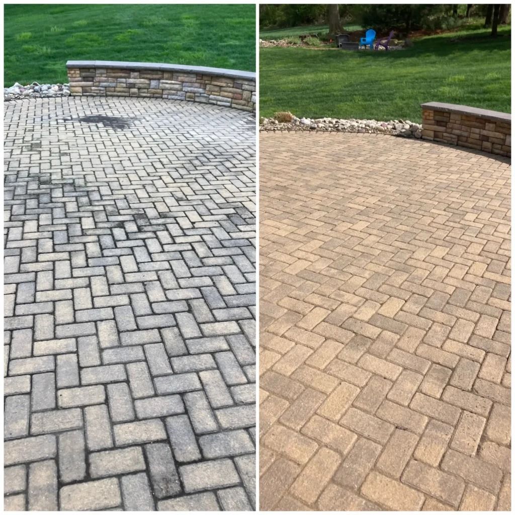 Side-by-side patio pavers: gray herringbone on left, tan brick pattern on right, beside a stone wall and lawn