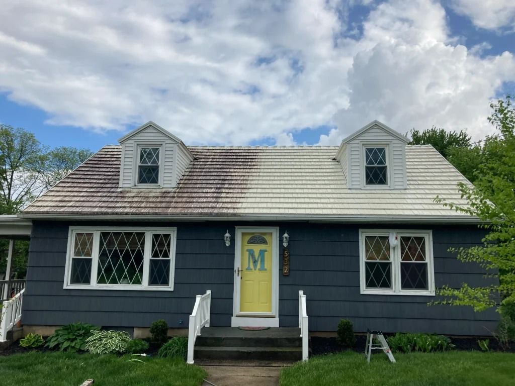 Small gray house with a yellow door, white dormers, and black shutters under a cloudy sky.
