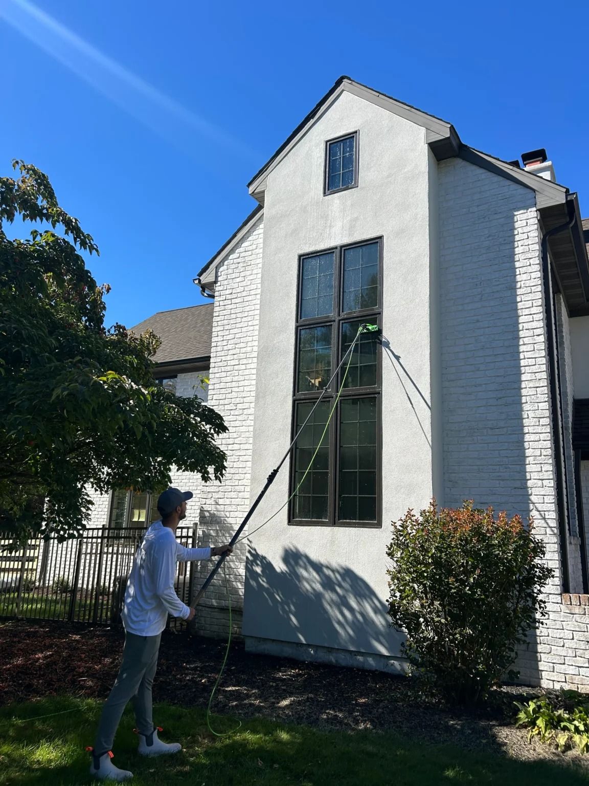 Person on a ladder cleaning a tall window on a white house outside