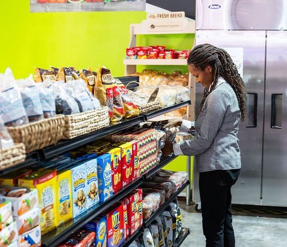 Woman shopping in a store, looking at the shelves of food. Green wall behind her.