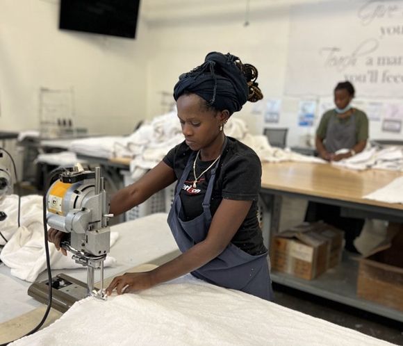 Woman cutting white fabric with a power cutter in a workshop. Another woman in the background.