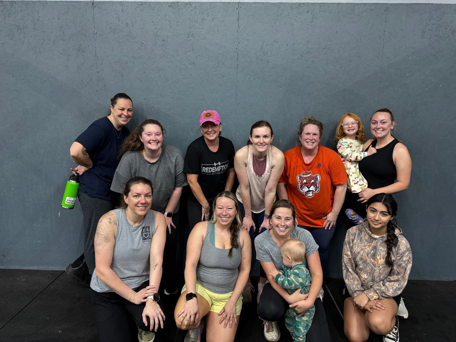 Nine people posing together in front of a gray wall, smiling after a workout session