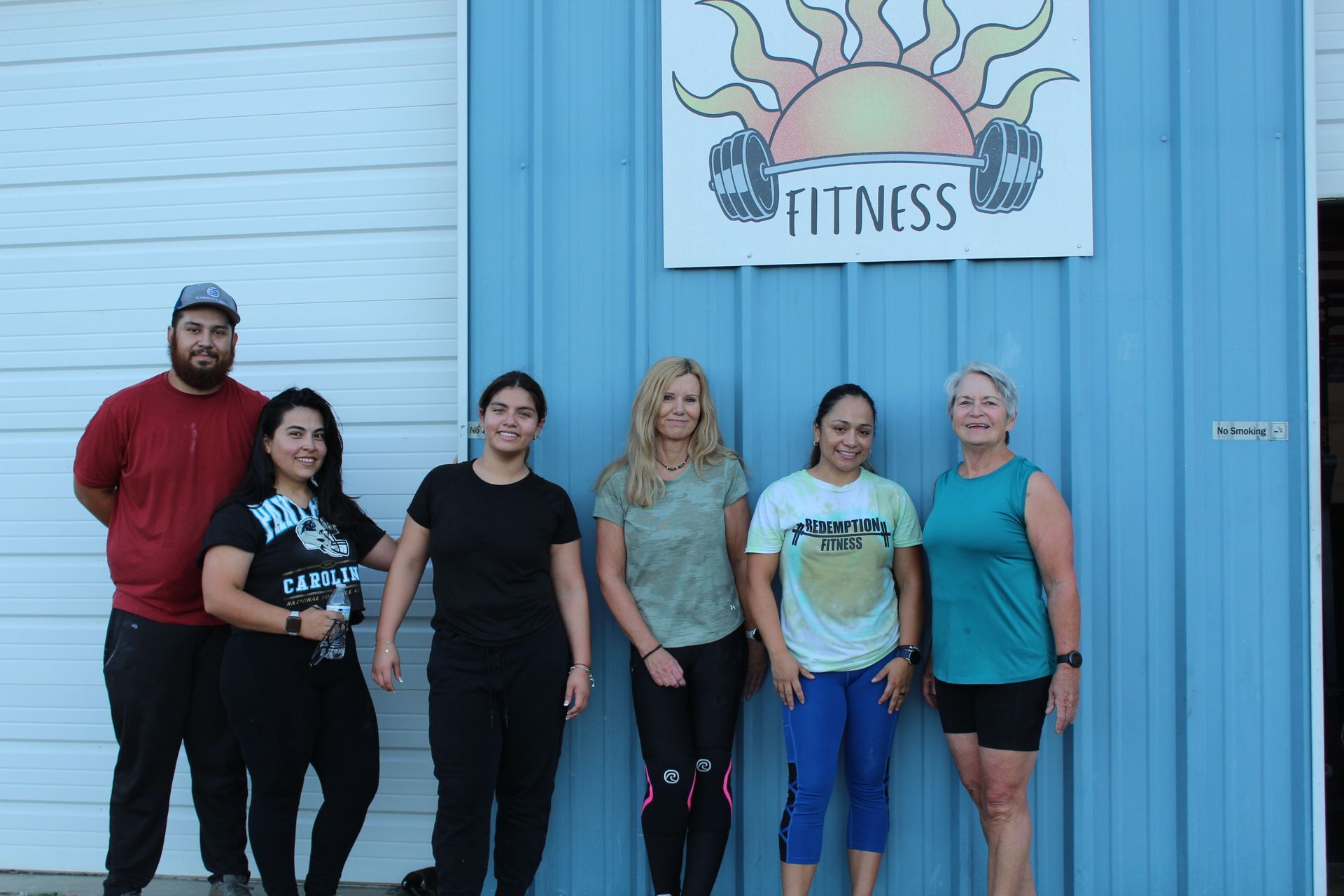 Five people stand outside a fitness studio beneath a “FITNESS” sign.