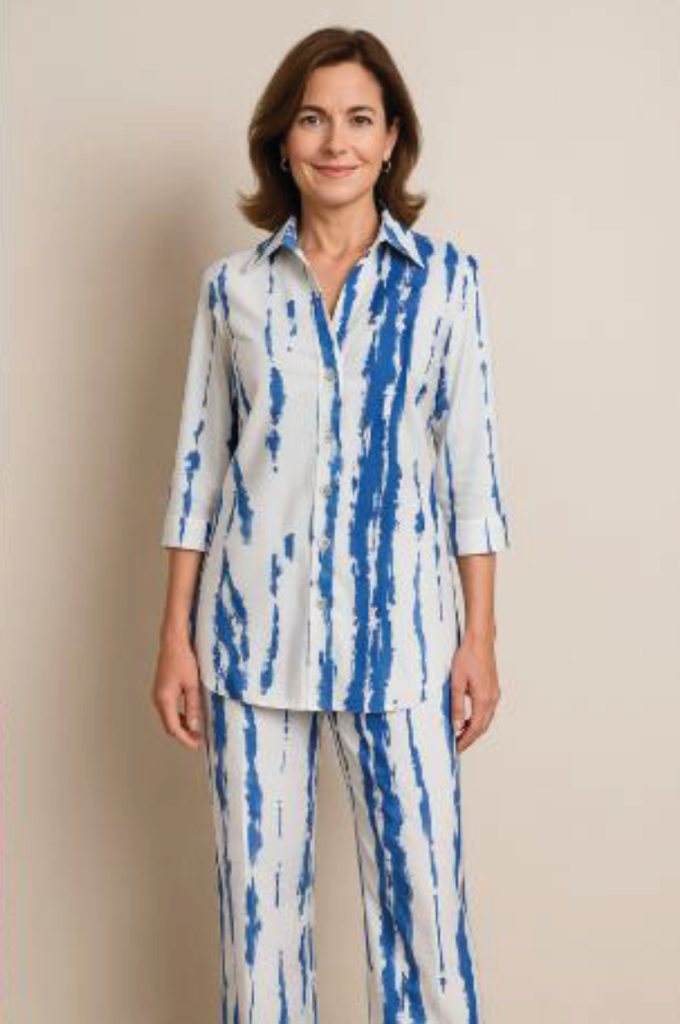 Mujer de pie con túnica y pantalones estampados en blanco y azul sobre un fondo beige liso.