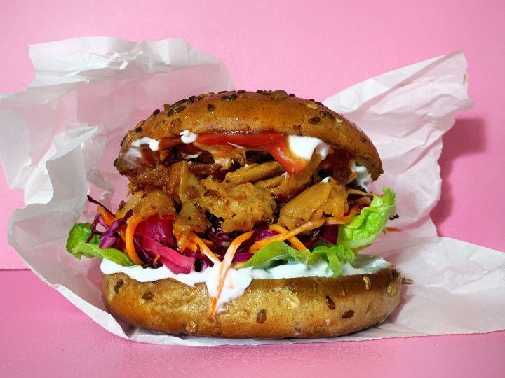 Sesame bun burger with lettuce, tomato, onion, sauce, and fried filling on pink background