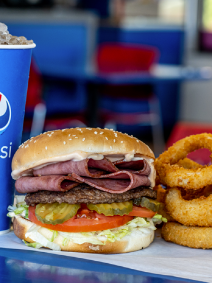 Roast beef sandwich with onion rings and a Pepsi cup on a table