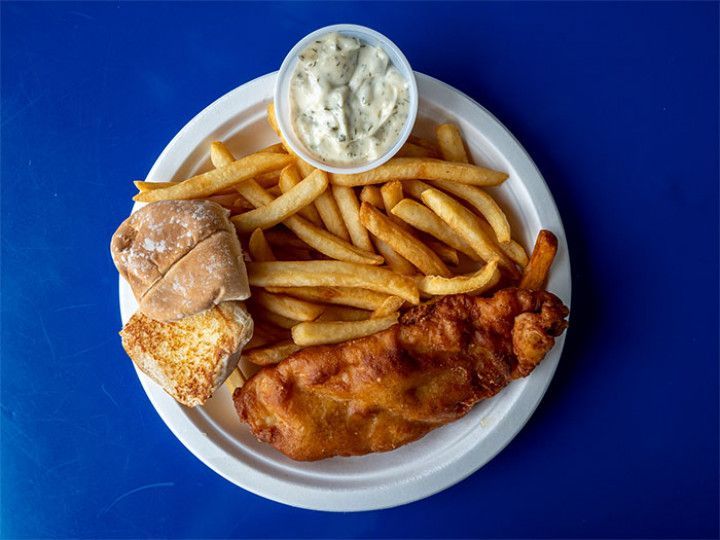 Plate of fish and chips with fries, tartar sauce, and bread on a blue table