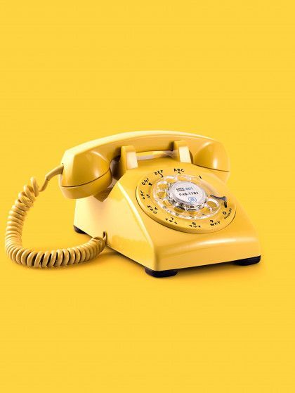Yellow rotary telephone on a bright yellow background with the handset resting on top