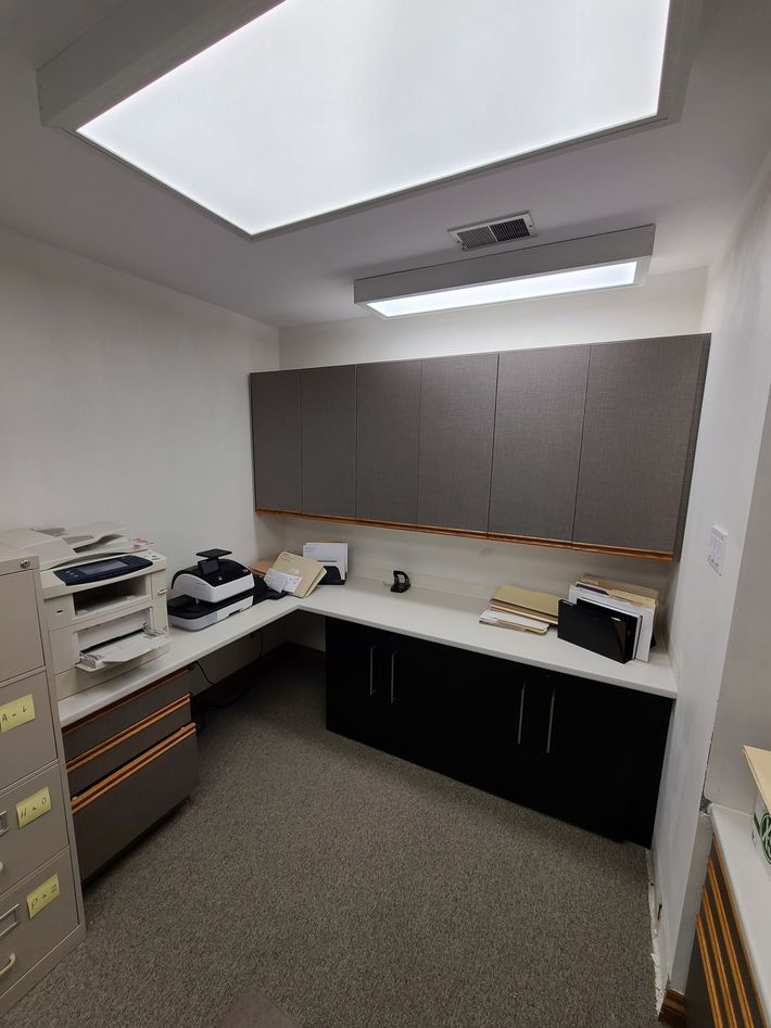 wrapped Office space with built-in desk, cabinets, and overhead lighting; filing cabinet on left.