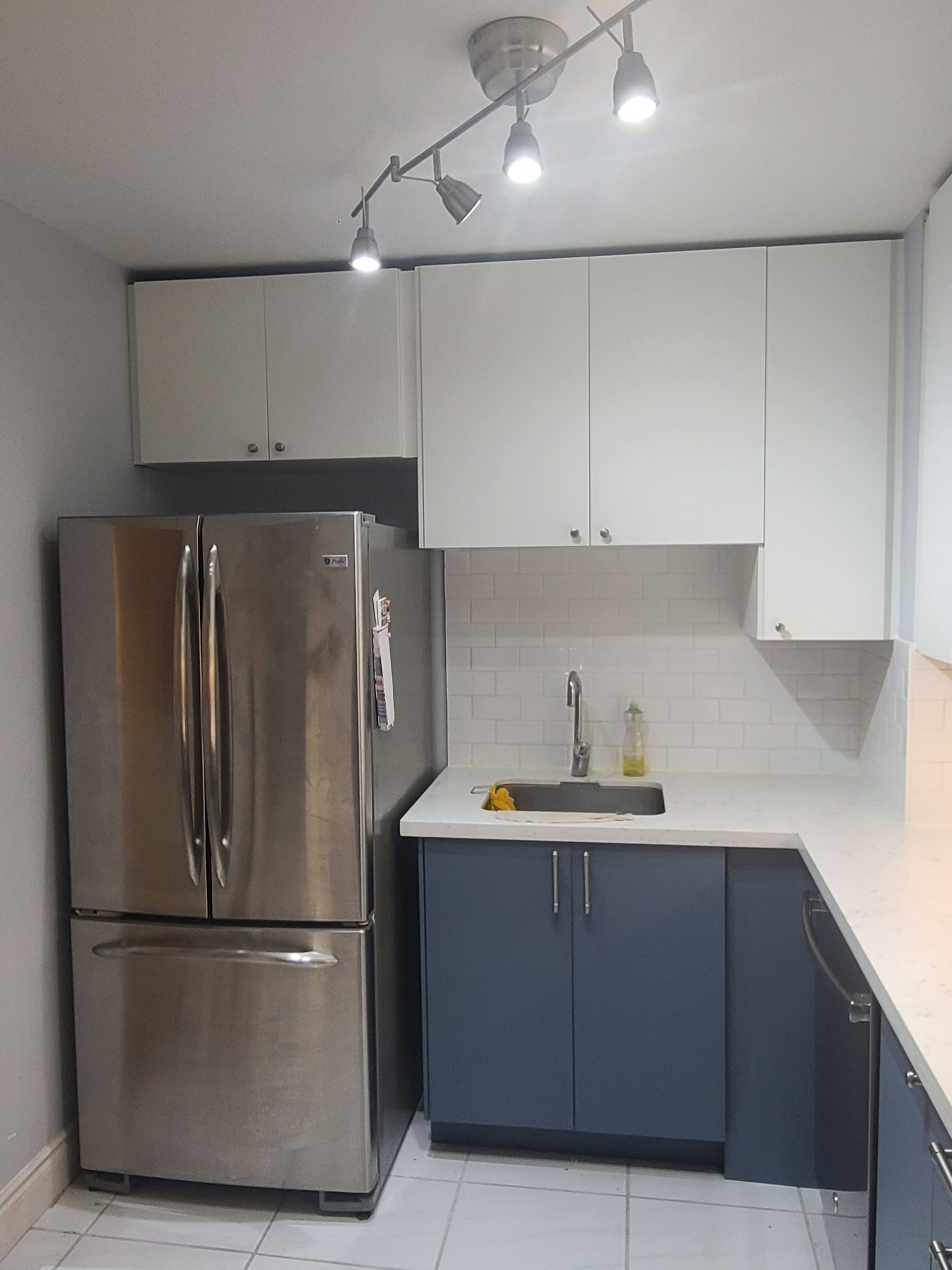 Small kitchen with stainless steel fridge, white upper cabinets, and blue lower cabinets.