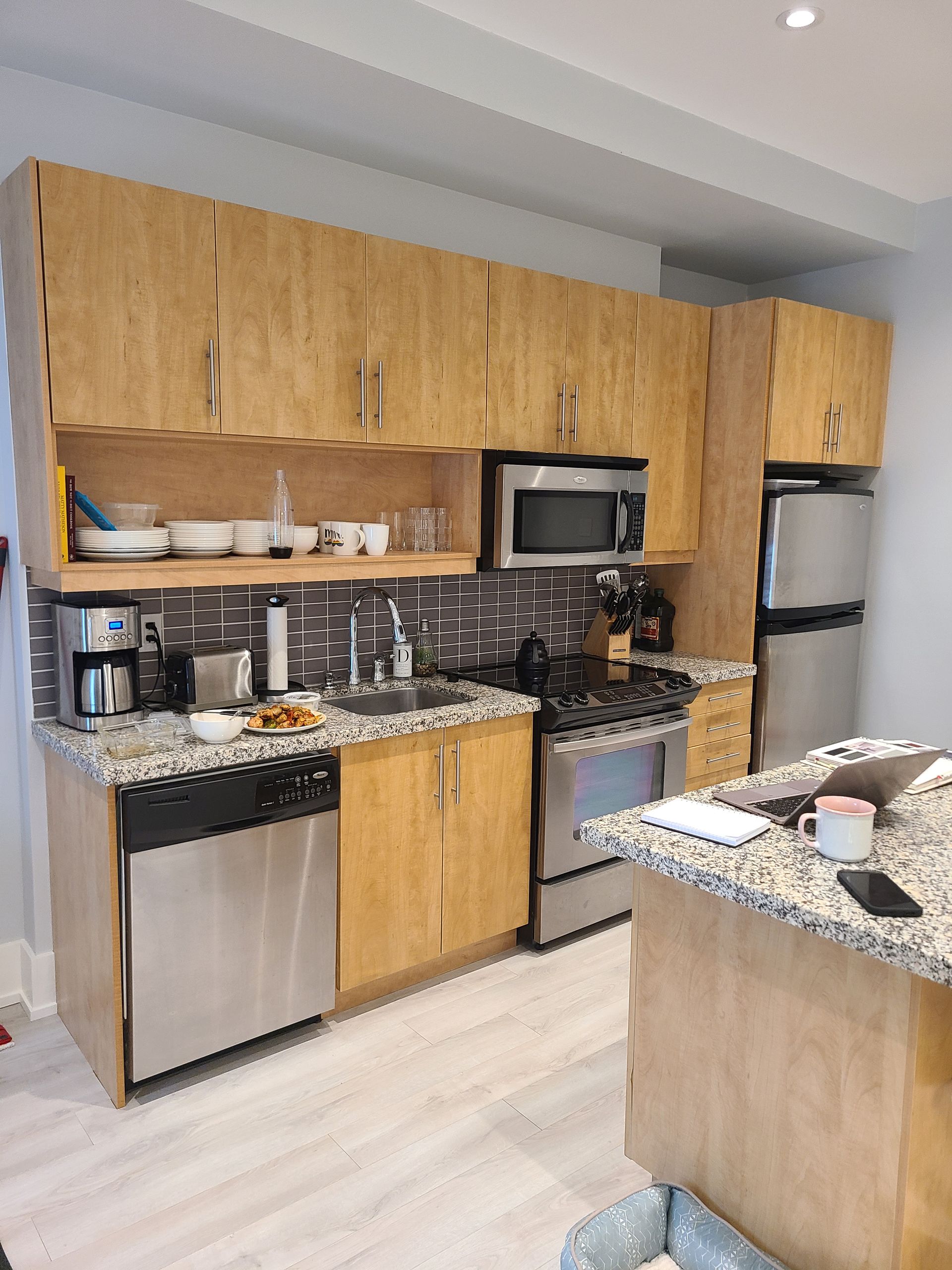 Kitchen with light wood cabinets, stainless steel appliances, and a granite countertop island.