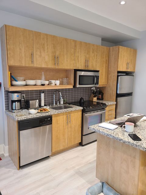 Kitchen with light wood cabinets, stainless steel appliances, and a granite countertop island.