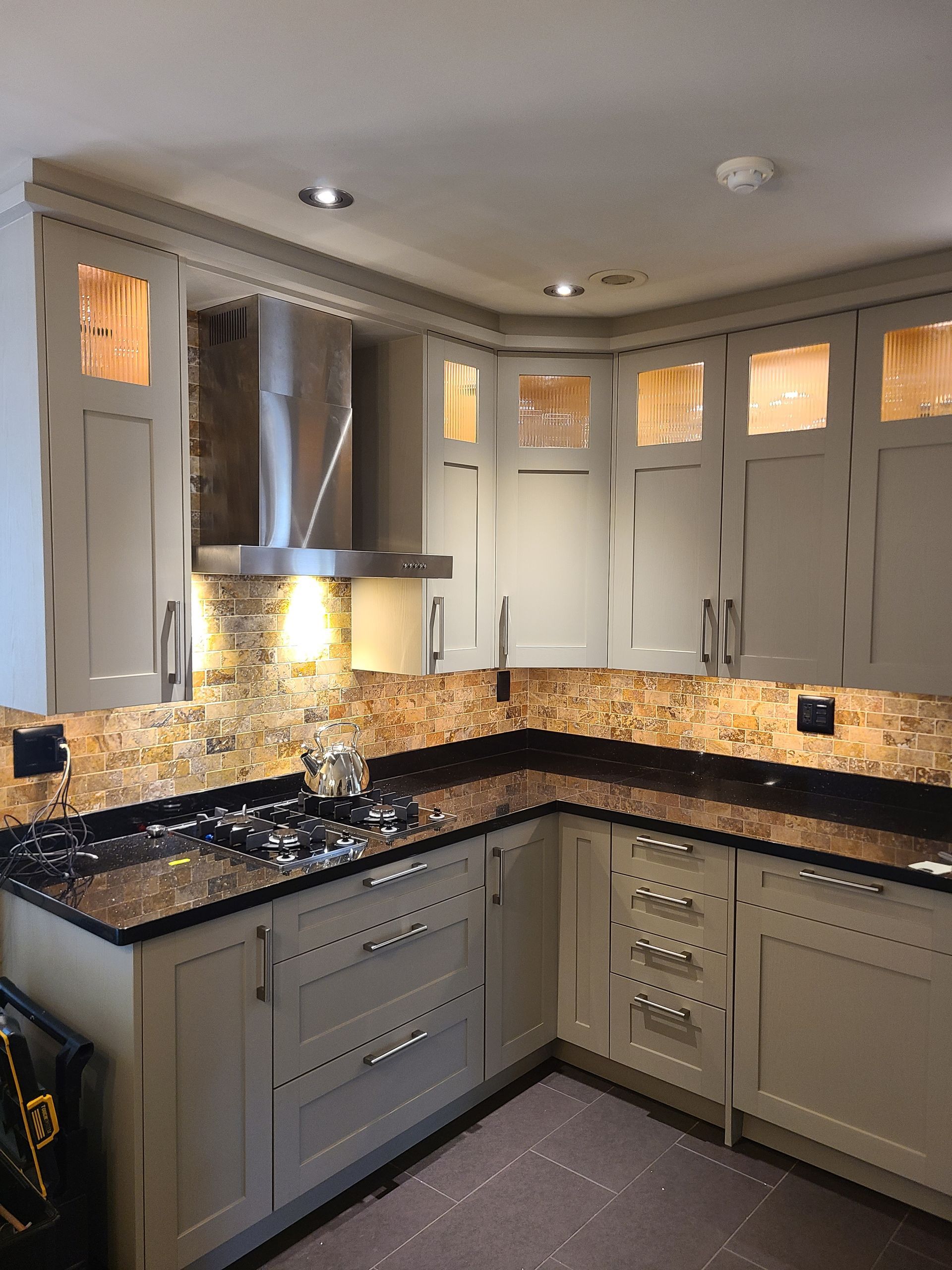 Beige kitchen with stainless steel range hood, dark countertops, and cabinets with glass inserts.