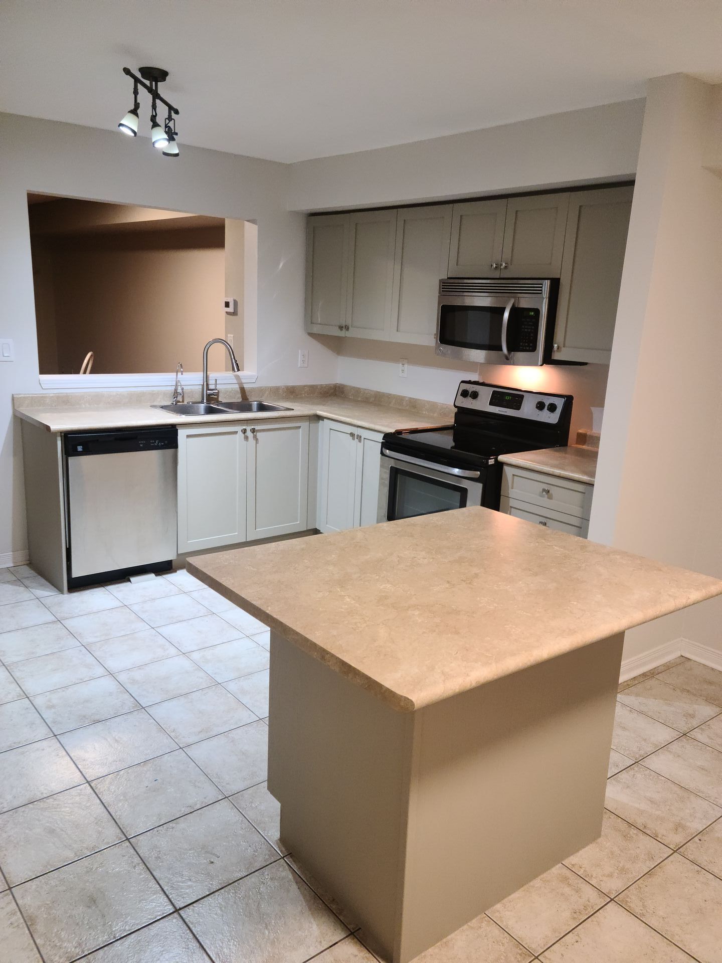 Kitchen with beige cabinets, stainless steel appliances, and island with a light-colored countertop.