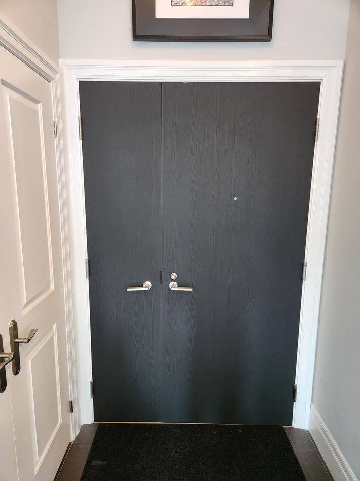 Black door with silver handles, doormat, white trim and frame, under a framed picture.