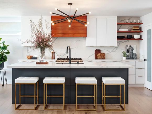Modern kitchen with island, white countertops, dark cabinets, gold stools, and sputnik chandelier.