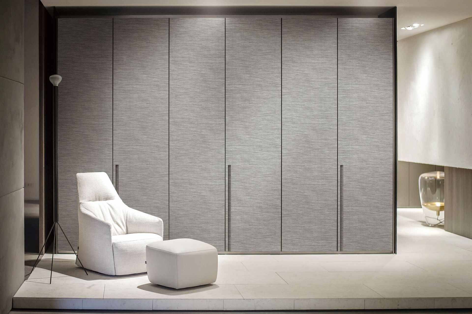 Cozy interior: White chair and ottoman in front of textured gray closet doors. Neutral color palette.